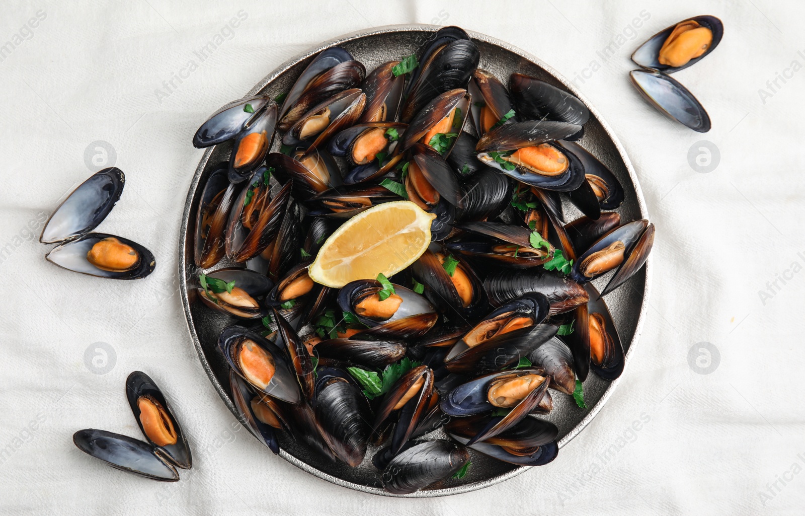 Photo of Plate with cooked mussels, parsley and lemon on white tablecloth, flat lay