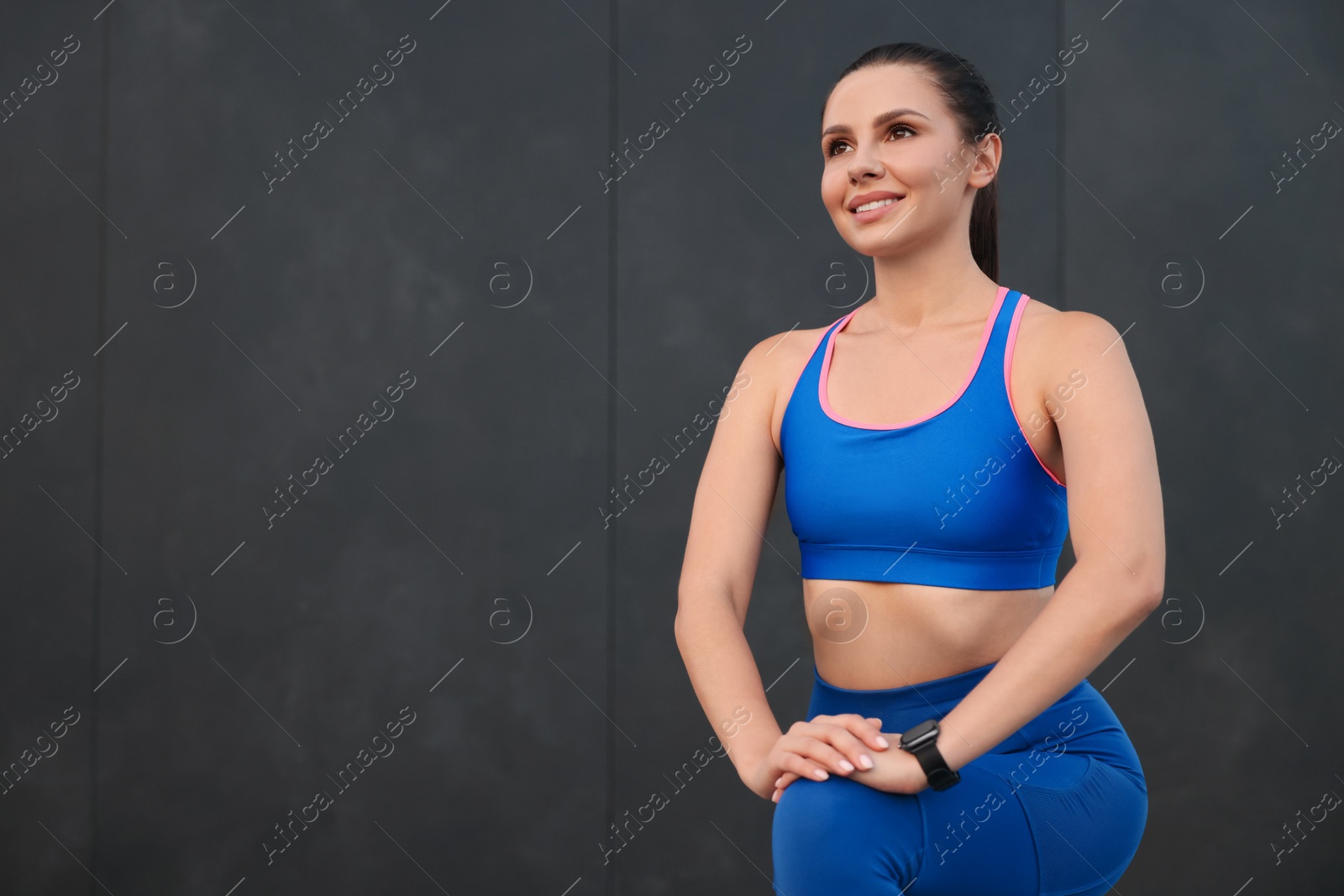 Photo of Beautiful woman in stylish sportswear doing exercises near black wall. Space for text