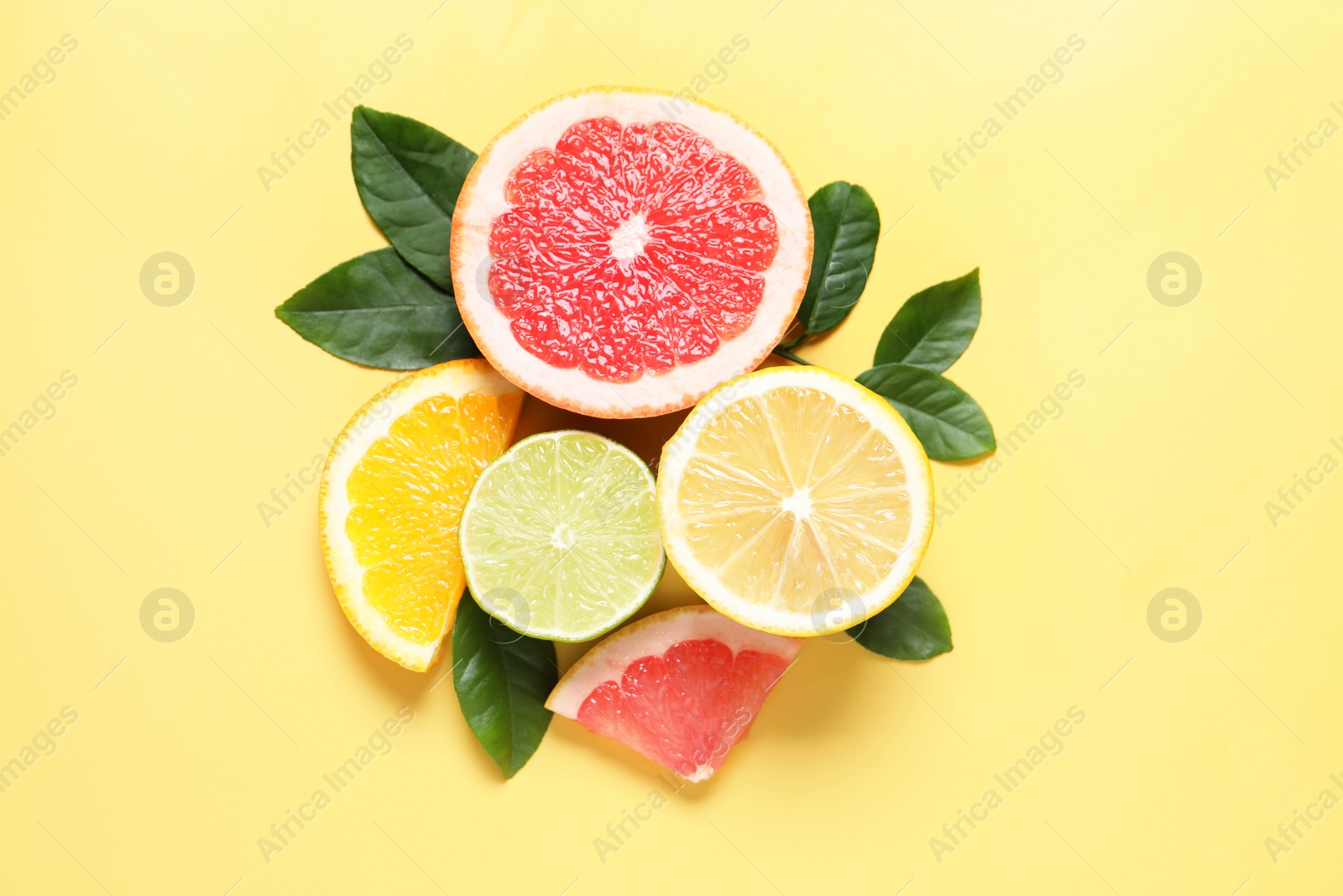 Photo of Different cut citrus fruits and leaves on yellow table, flat lay