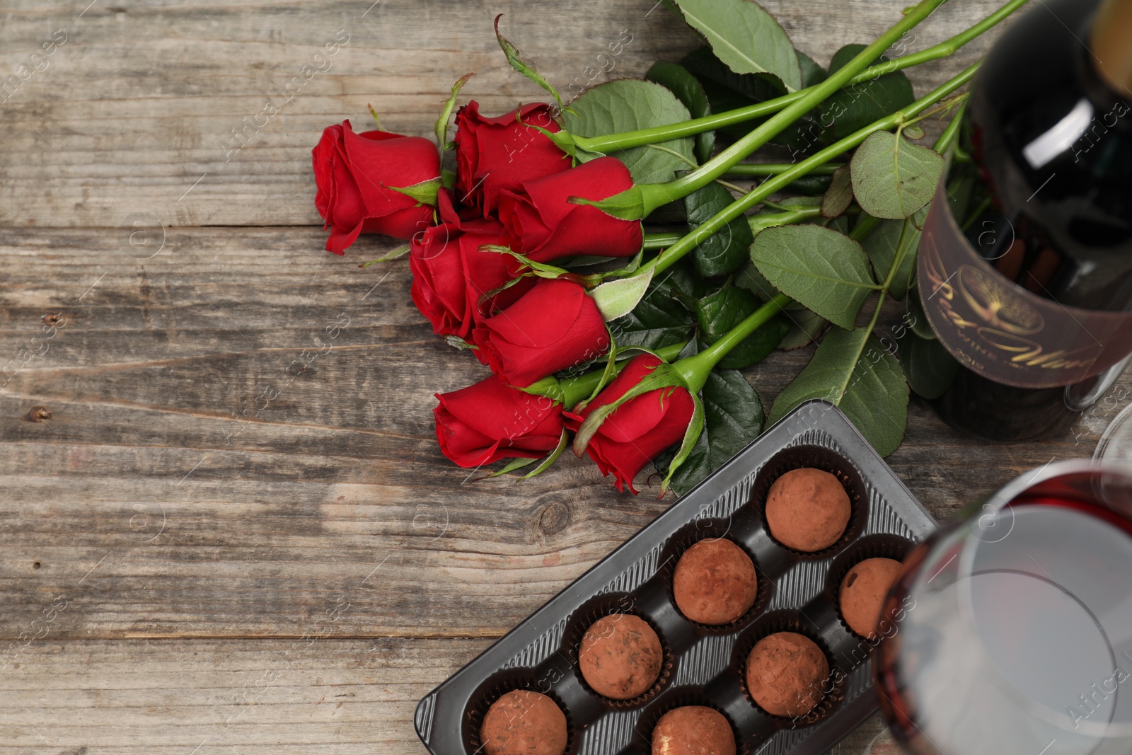 Photo of Red wine, chocolate truffles and roses on wooden table, flat lay. Space for text