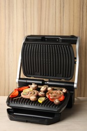 Photo of Electric grill with homemade sausages, mushrooms and bell pepper on wooden table