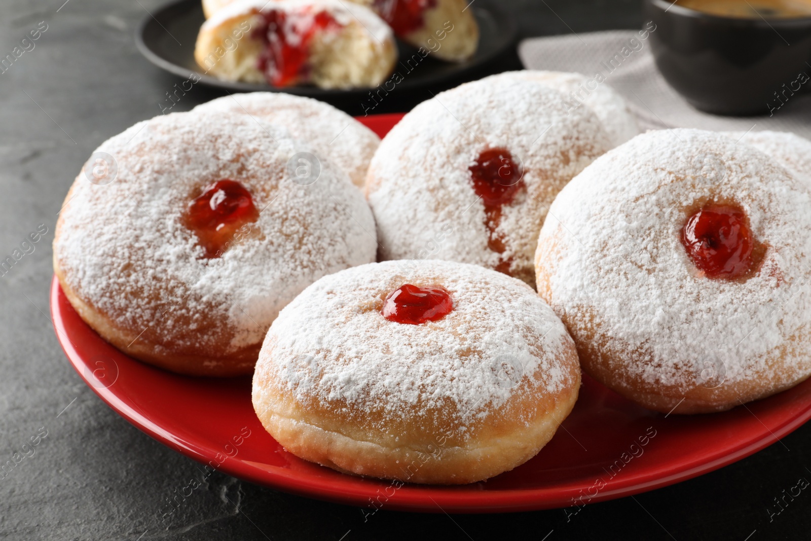 Photo of Delicious donuts with jelly and powdered sugar on black table, closeup