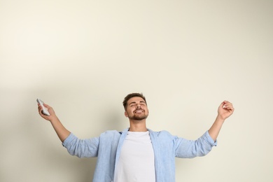 Happy young man with air conditioner remote control on beige background