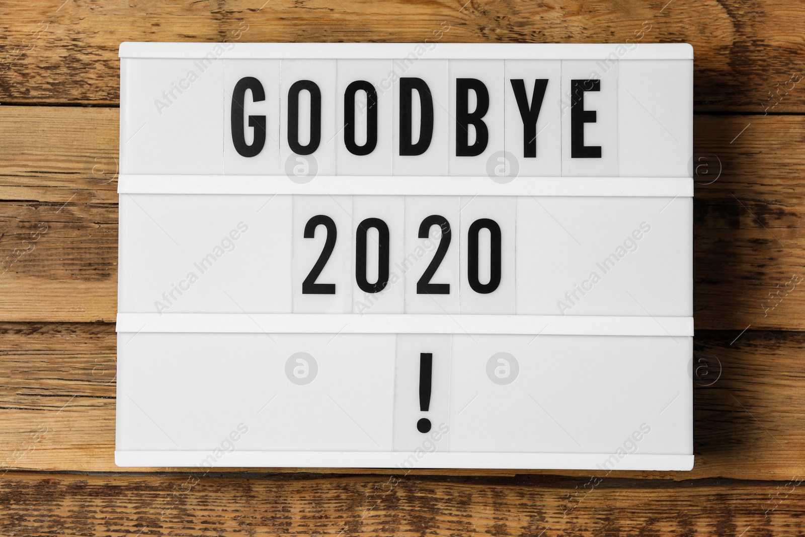 Photo of Lightbox with phrase Goodbye 2020! on wooden table, top view