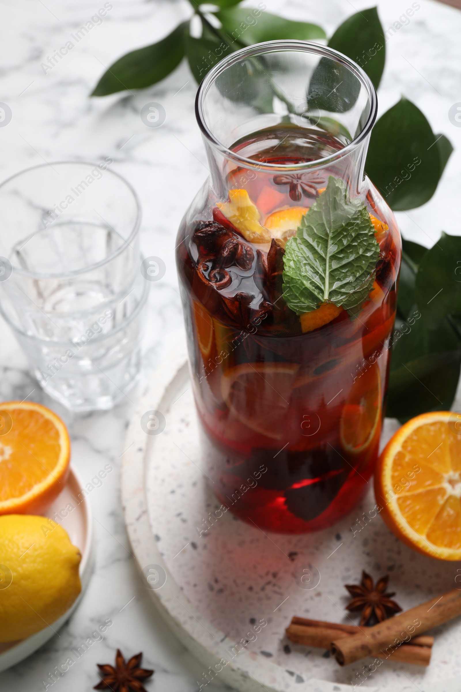 Photo of Delicious punch drink in bottle, spices and citrus fruits on white marble table