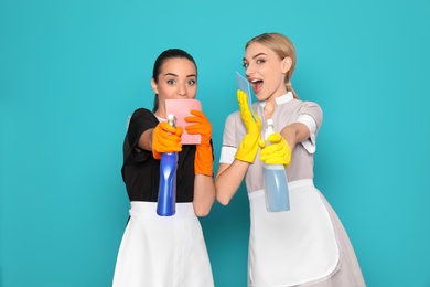 Young chambermaids with rags and detergents on color background