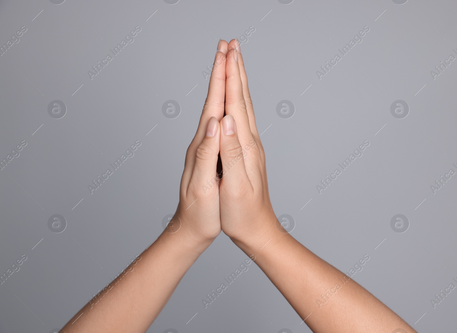 Photo of Woman holding hands clasped while praying against light grey background, closeup