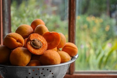 Colander with delicious ripe apricots near window. Space for text