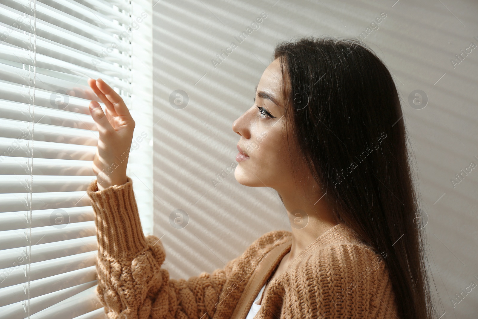 Photo of Young woman opening window blinds at home