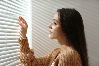 Photo of Young woman opening window blinds at home