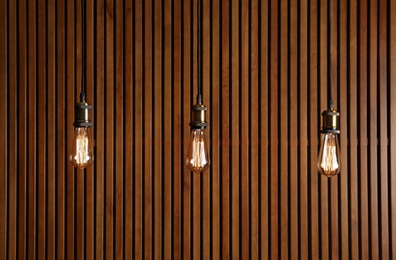 Photo of Hanging lamp bulbs in chandeliers near wooden wall