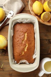 Photo of Tasty lemon cake in baking dish and citrus fruits on wooden table, flat lay