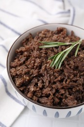 Photo of Fried ground meat in bowl and rosemary on white tiled table, closeup