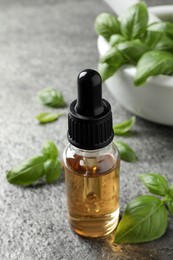 Photo of Glass bottle of basil essential oil and leaves on grey stone table