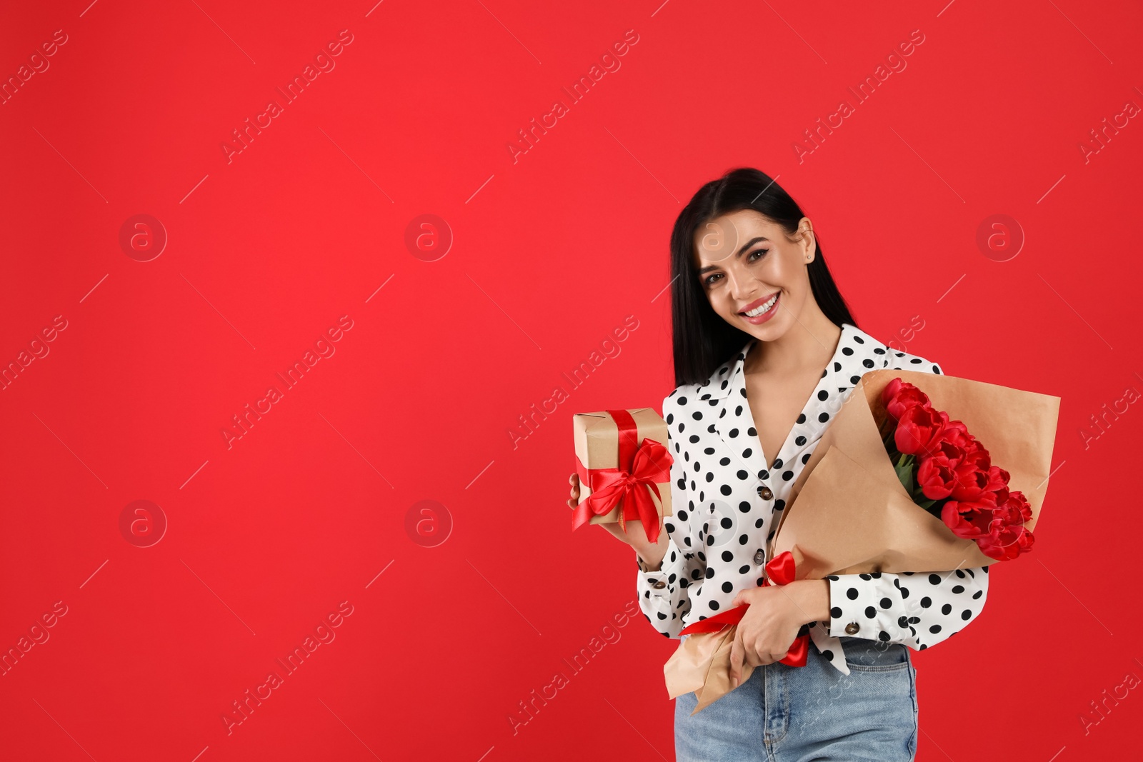 Photo of Happy woman with tulip bouquet and gift box on red background, space for text. 8th of March celebration