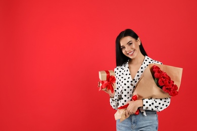 Happy woman with tulip bouquet and gift box on red background, space for text. 8th of March celebration
