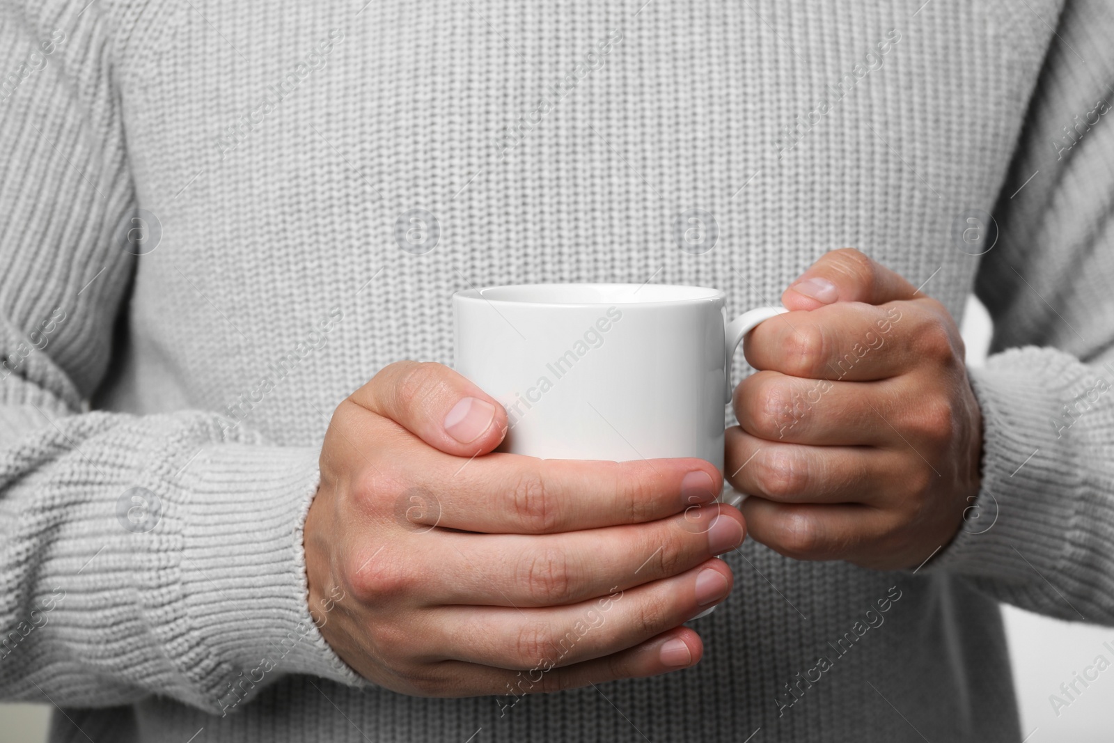 Photo of Man holding white mug on light grey background, closeup