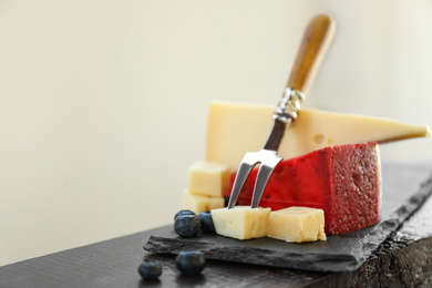 Photo of Different delicious cheeses, fork and blueberries on wooden railing. Space for text