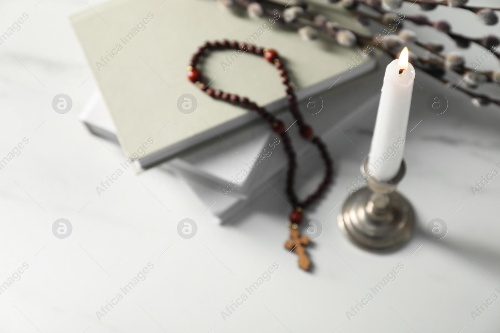 Photo of Books, burning candle and rosary beads on white table, closeup