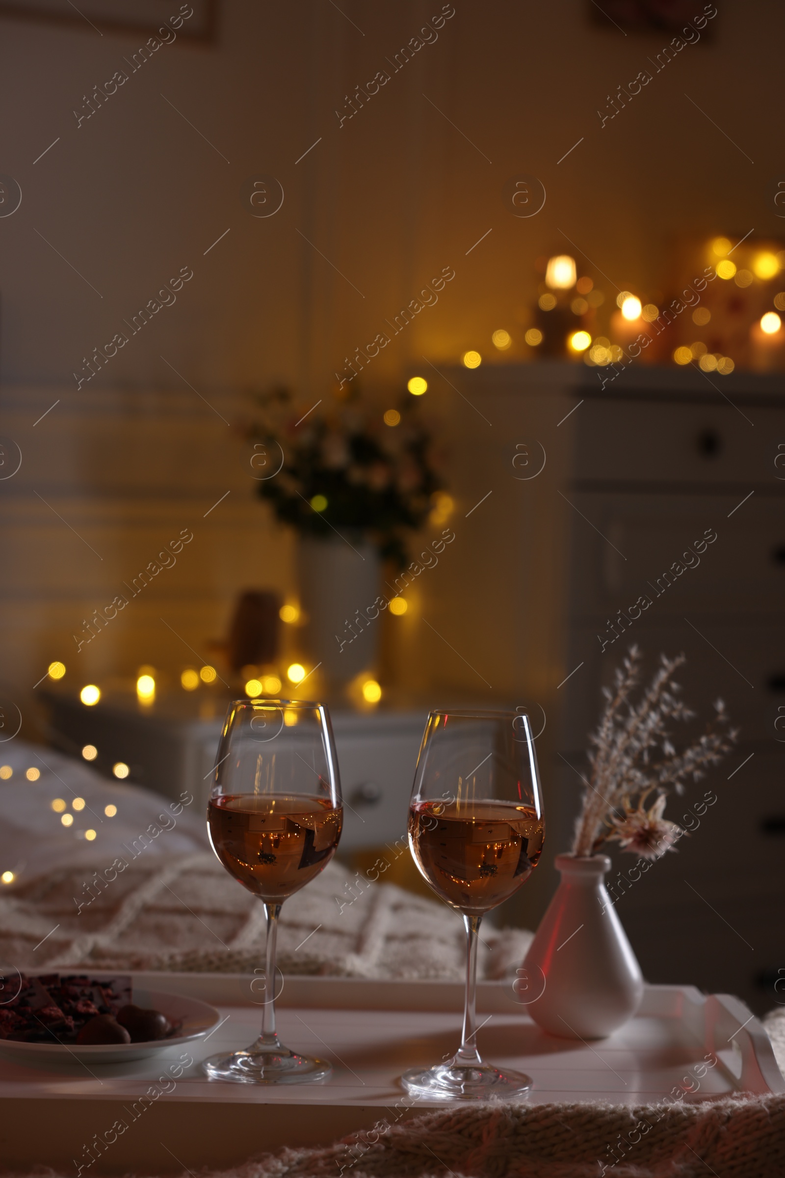 Photo of Glasses of wine in bedroom adorned for romantic evening. Space for text