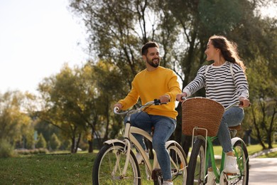 Beautiful couple riding bicycles in park, space for text