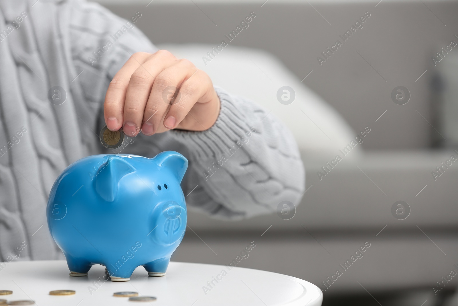 Photo of Man putting coin into piggy bank at white table, closeup. Space for text