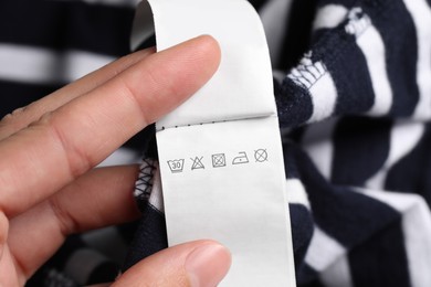 Photo of Woman holding clothing labels on striped garment, closeup