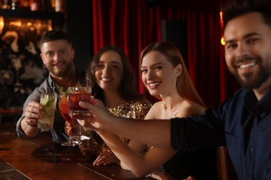 Photo of Happy friends clinking glasses with fresh cocktails at bar counter