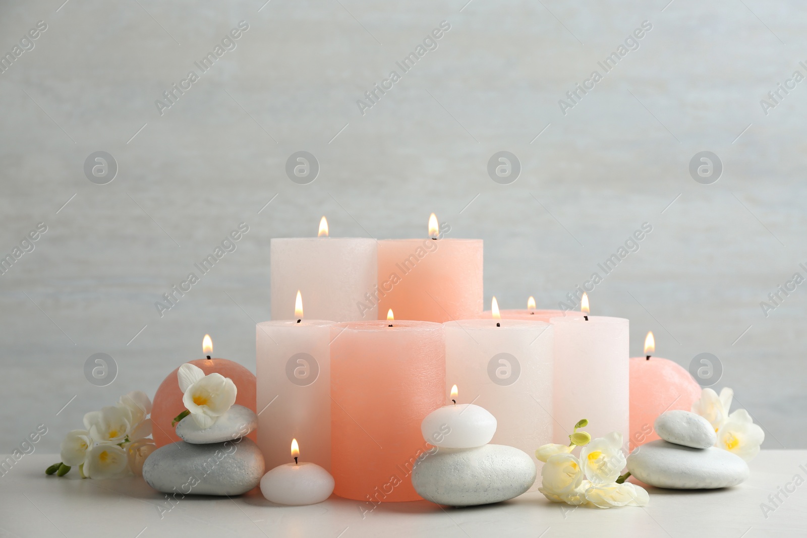 Photo of Beautiful composition with candles, stones and flowers on table against light background