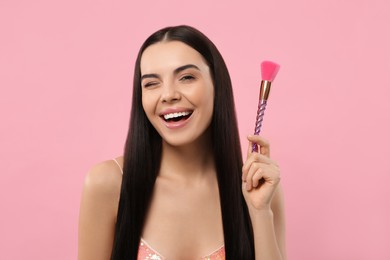 Photo of Happy woman with makeup brush on pink background