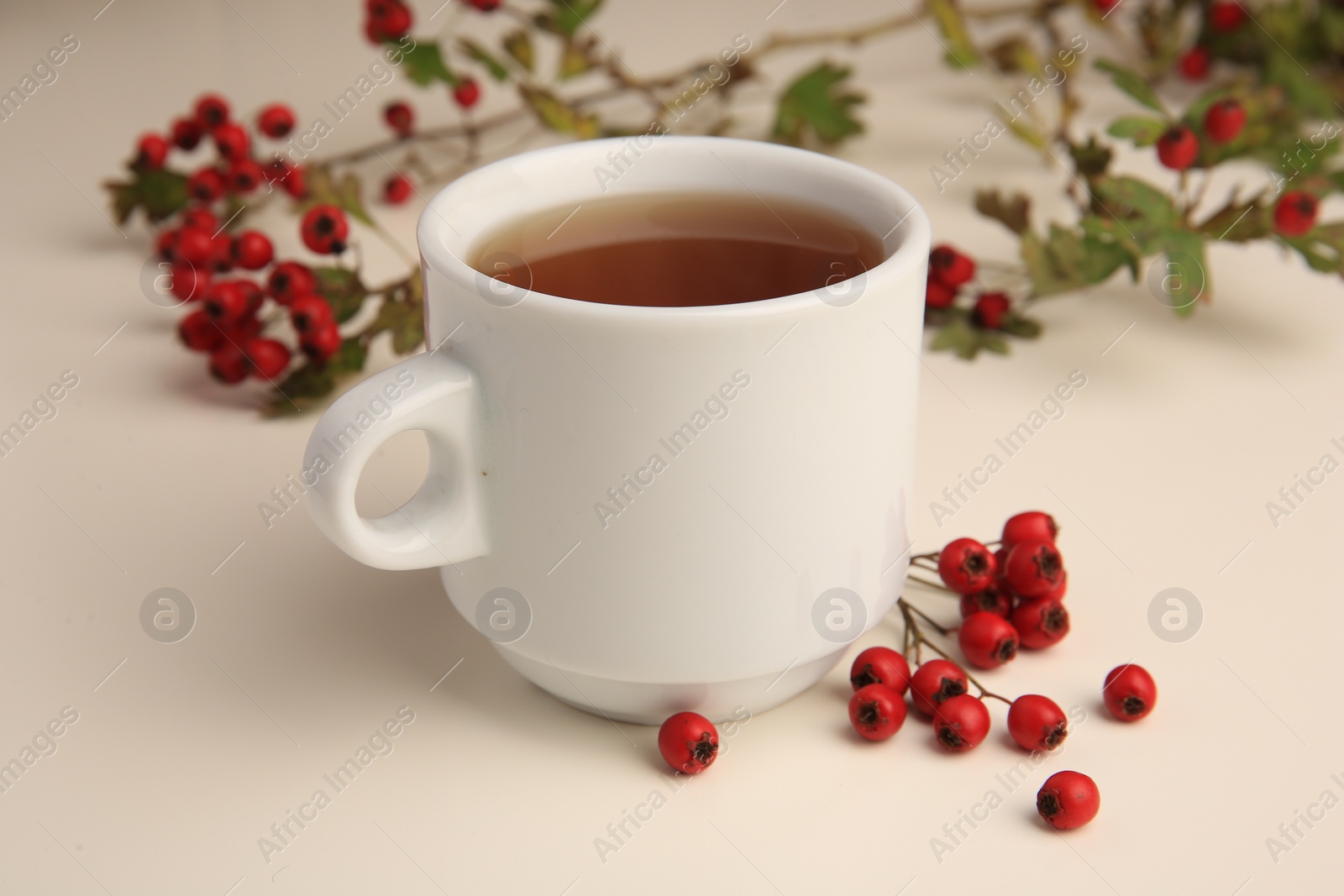 Photo of Aromatic hawthorn tea in cup and berries on beige table, closeup