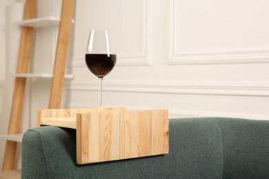 Glass of red wine on sofa with wooden armrest table in room, space for text. Interior element