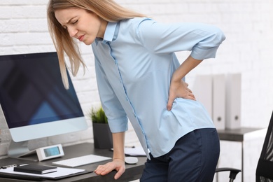 Photo of Young woman suffering from back pain in office