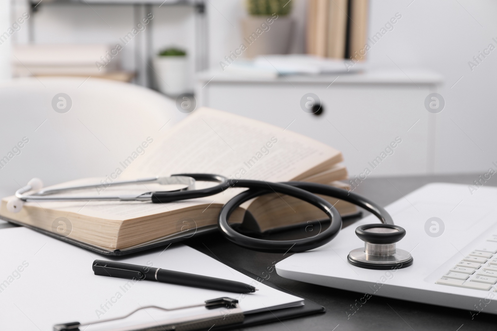 Photo of Open student textbook, clipboard and stethoscope near laptop on grey table indoors, closeup. Medical education