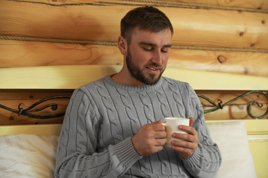 Young man in warm sweater with cup of hot drink at home