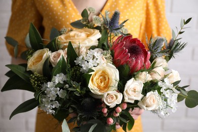 Photo of Woman with bouquet of beautiful roses near white brick wall, closeup