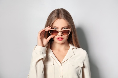 Photo of Young woman wearing stylish sunglasses on light background