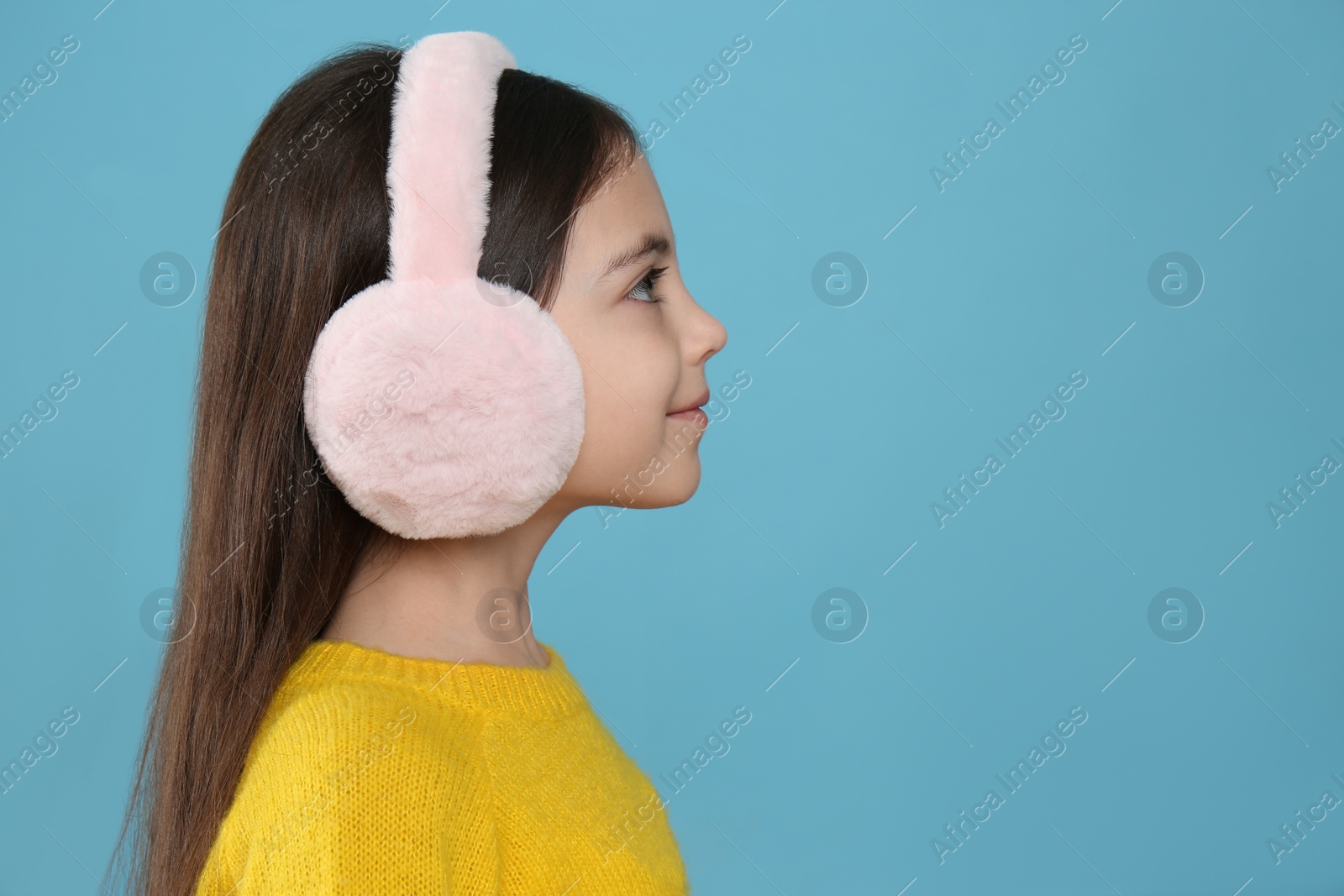 Photo of Cute little girl wearing stylish earmuffs on light blue background. Space for text