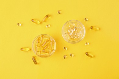 Photo of Different vitamin capsules in glass bowls on yellow background, flat lay