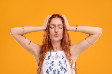 Beautiful young hippie woman sending air kiss on orange background