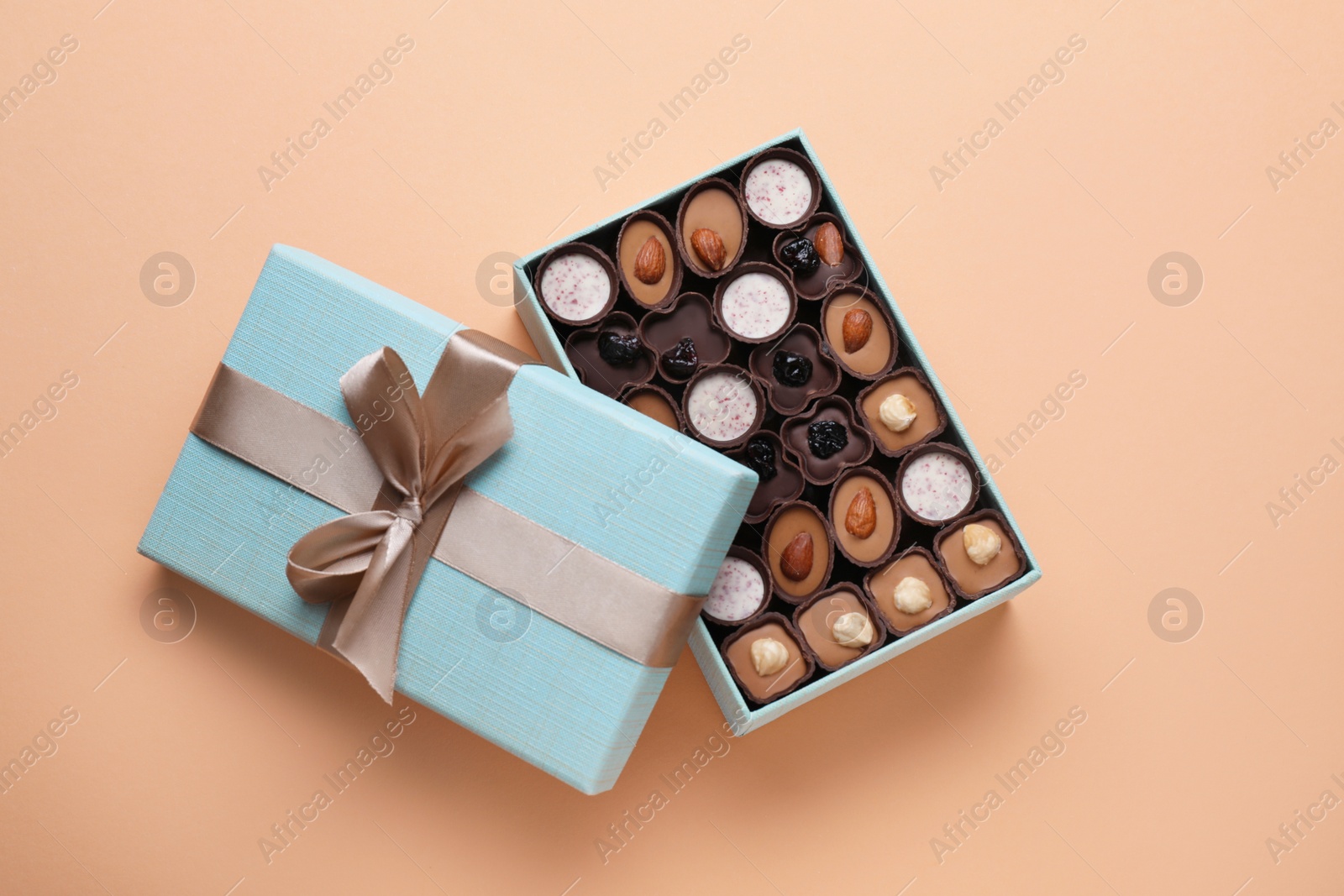 Photo of Open box of delicious chocolate candies on beige background, flat lay