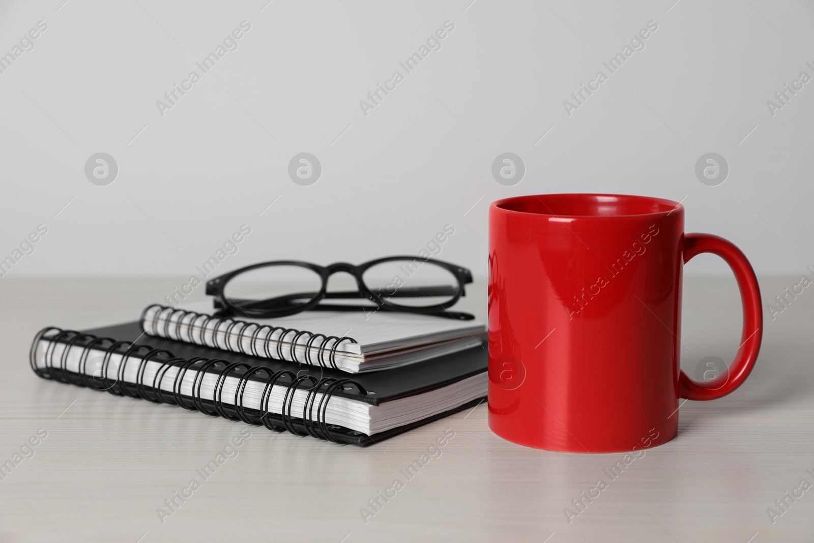 Red ceramic mug, stationery and glasses on white wooden table Photo of Red ceramic mug, stationery and glasses on white wooden table