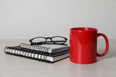 Photo of Red ceramic mug, stationery and glasses on white wooden table