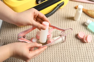 Woman putting small bottle with personal care product into plastic bag, closeup. Cosmetic travel kit