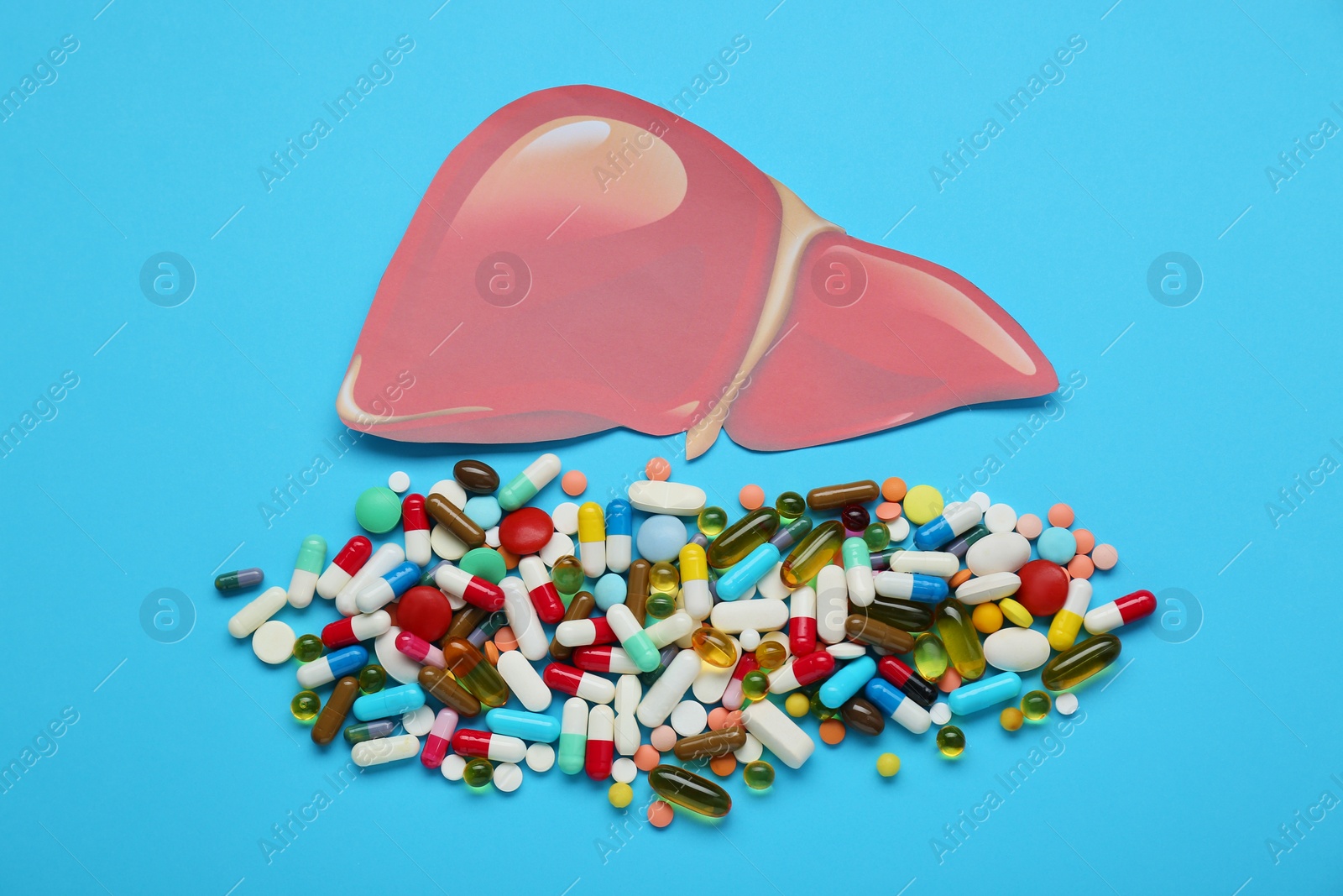 Photo of Paper liver and pills on light blue background, flat lay. Hepatitis treatment