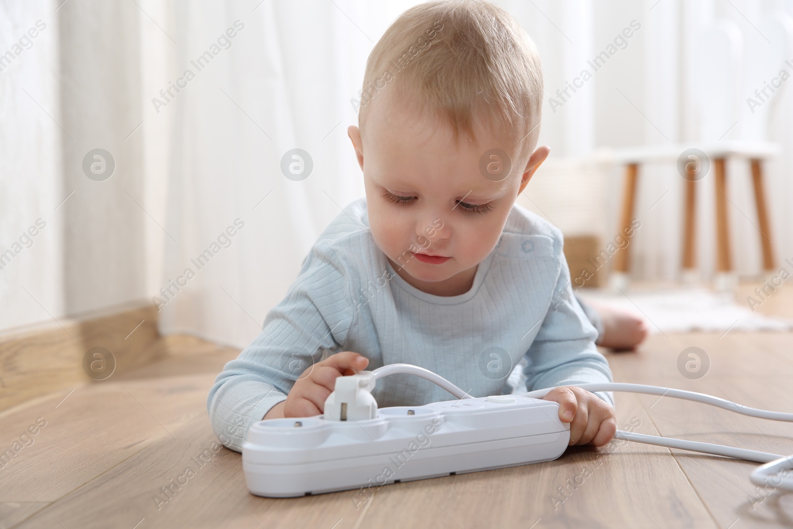 Photo of Little child playing with power strip and plug on floor indoors. Dangerous situation