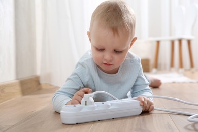 Photo of Little child playing with power strip and plug on floor indoors. Dangerous situation