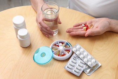 Photo of Woman with pills, organizer and glass of water at light wooden table, closeup