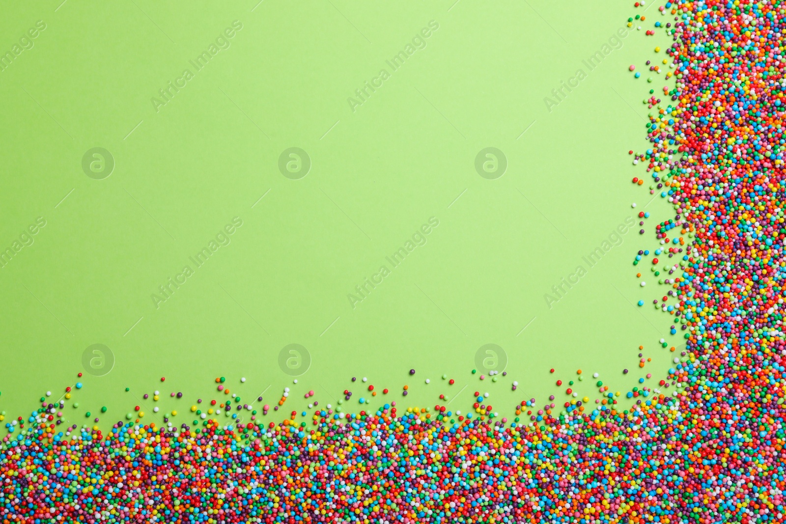 Photo of Colorful sprinkles on green background, flat lay with space for text. Confectionery decor