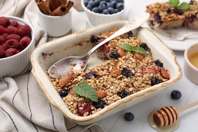 Photo of Tasty baked oatmeal with berries and almonds in baking tray on white table